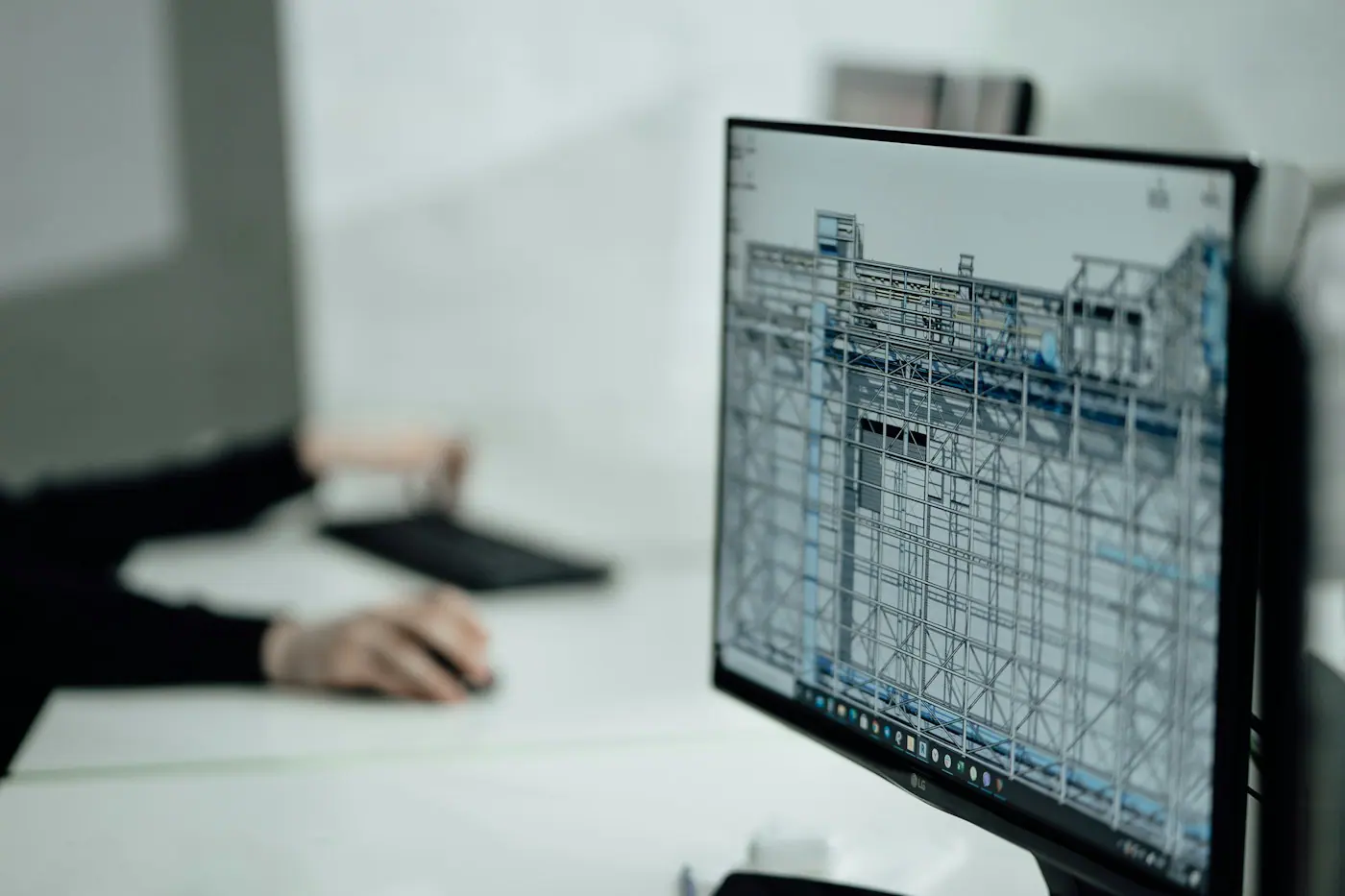 Ayrıntılı üç boyutlu yapı modeli gösteren monitörün yanında klavye ve fareyle çalışan eller