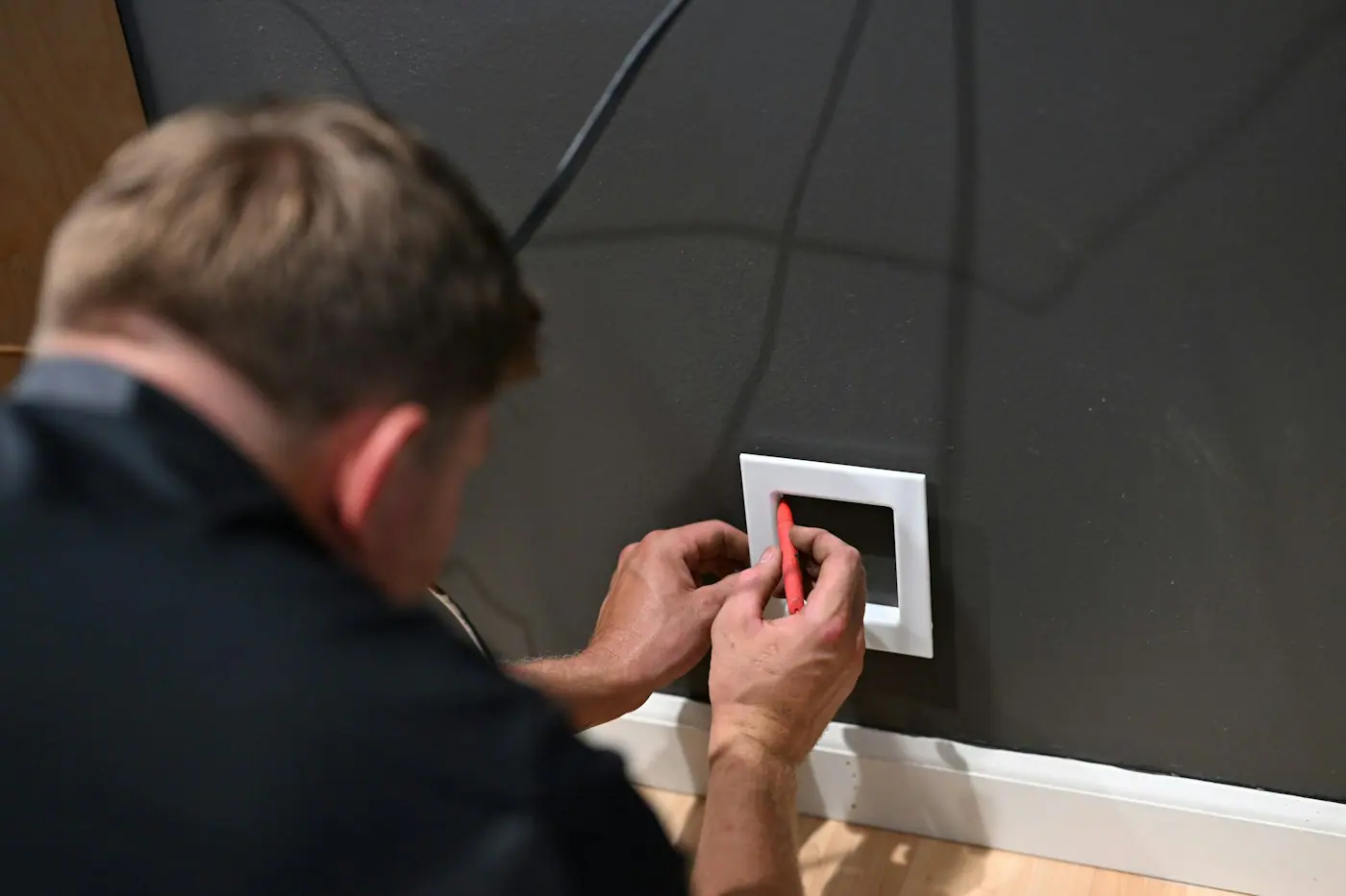Technician fitting a white electrical wall plate onto a dark grey interior wall