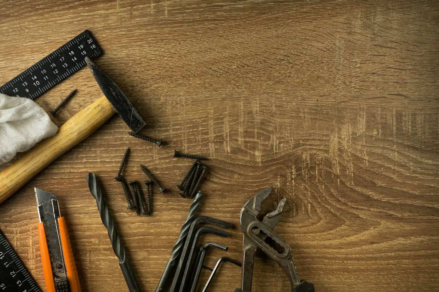 مطرقة وزاوية قياس وسكين قاطع ولقم مثقاب ومسامير ومفاتيح ألن وكماشة على خشب البلوط