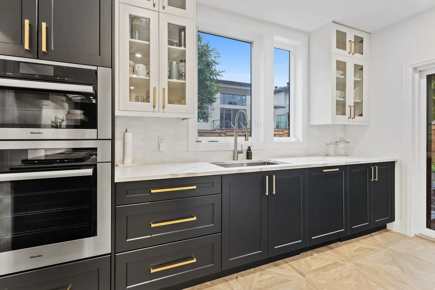 Charcoal kitchen cabinets with brass pulls, white worktop, built-in ovens and glass-front units