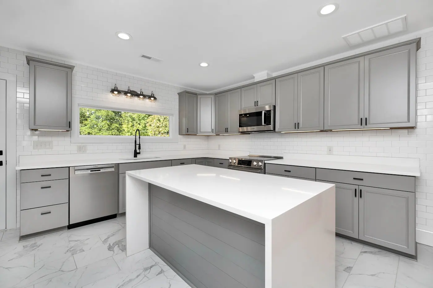 Newly finished kitchen with grey cabinets, white island, subway tiles and marble-look floor