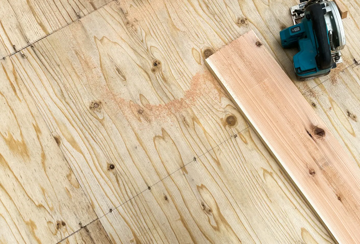 Light solid wood floorboard resting on a plywood subfloor beside a circular saw