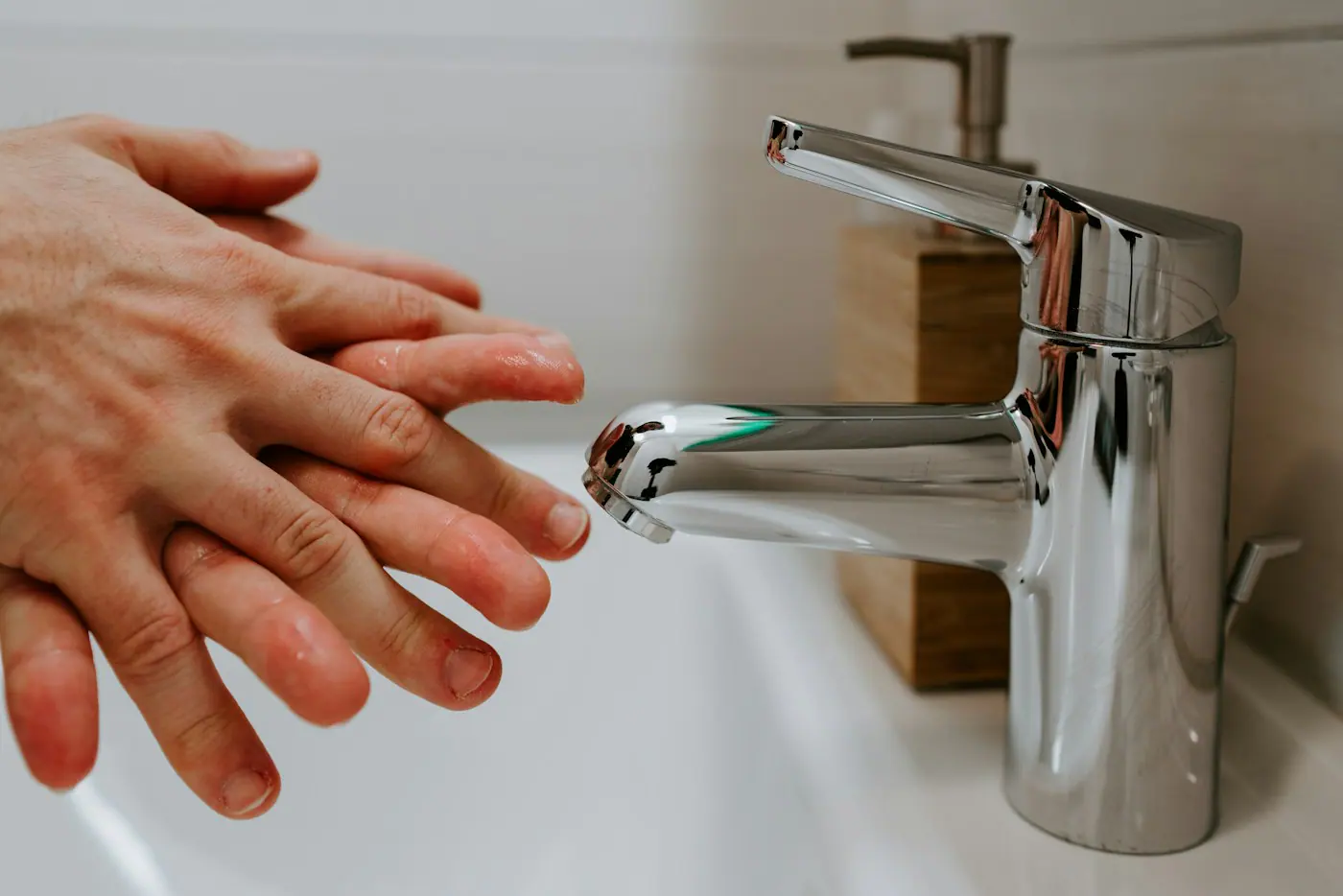 Beyaz banyo lavabosunda parlak krom tek kollu batarya ve eller