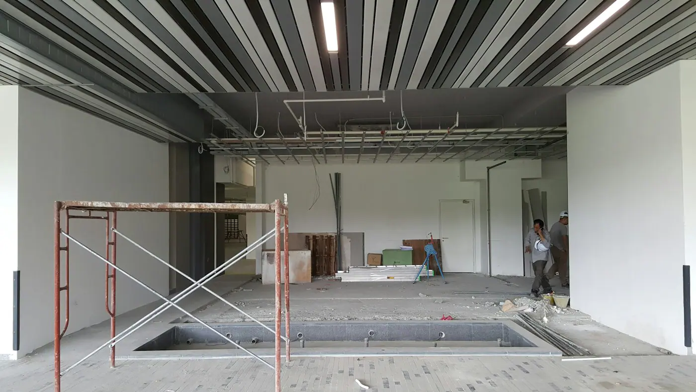 Large commercial interior under construction with scaffolding, exposed ceiling services and workers